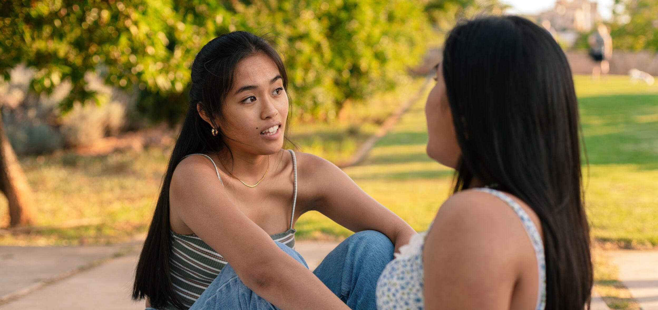 Two women facing each other, talking while they sit in the grass