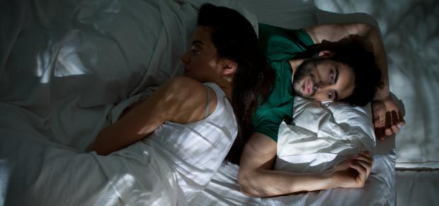 Man awake in bed while his partner sleeps