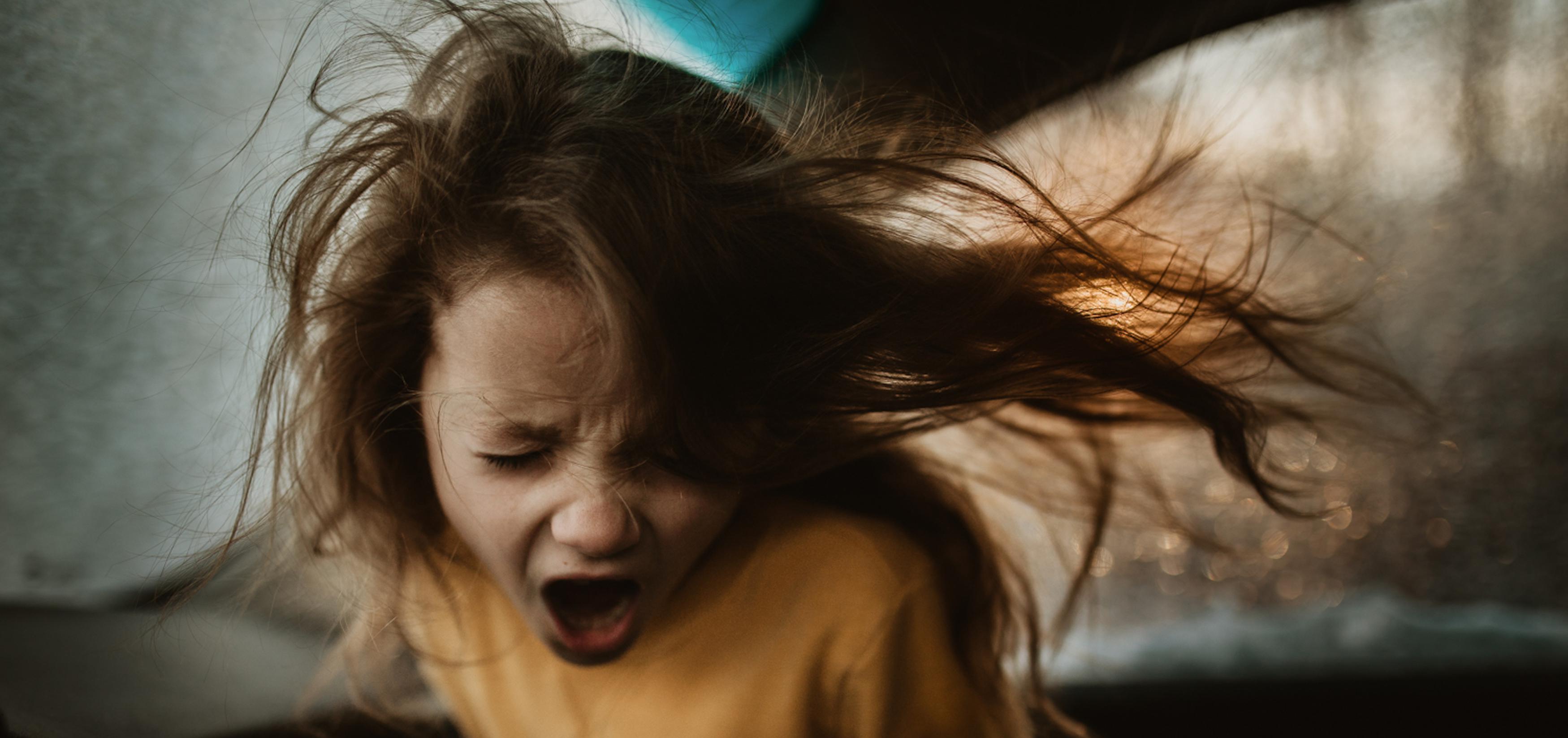 A young girl yelling with a scrunched face with her hair blowing in the wind