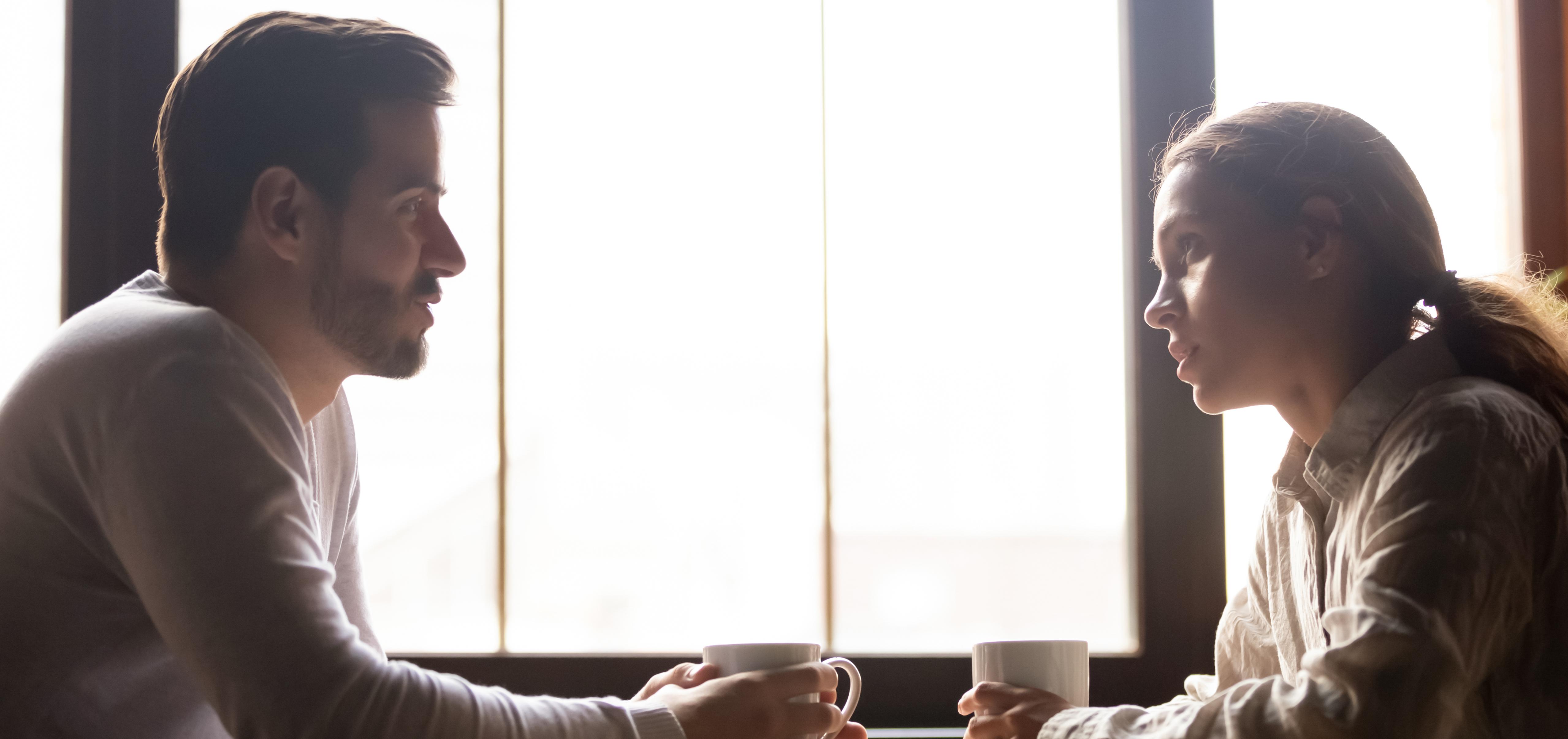 two people sit across from each other at a table, in serious conversation