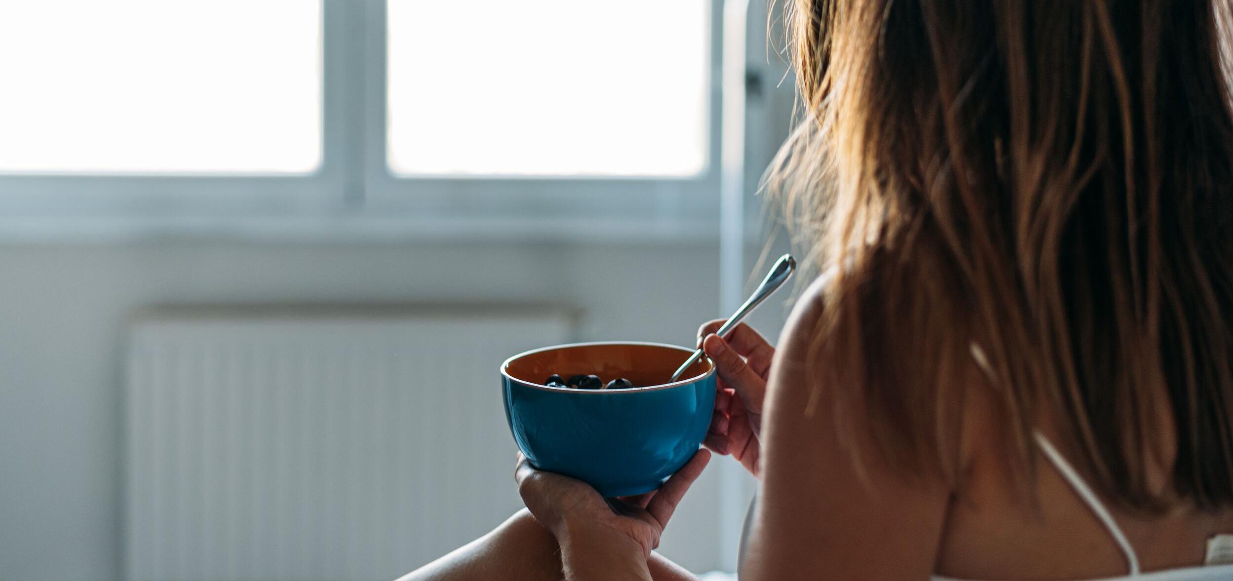 Person holding a spoon and blue and red bowl full of blueberries